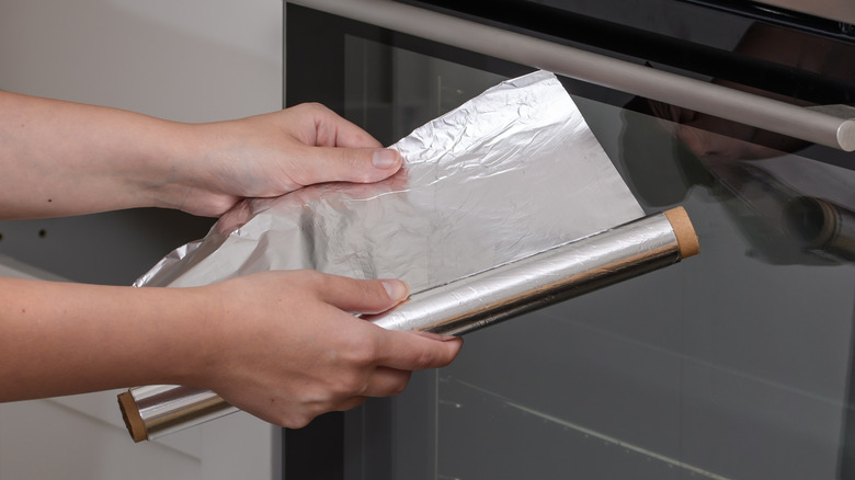 person holding a roll of aluminum foil in front of oven
