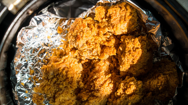 Fried chicken pieces sitting in an aluminum foil-lined air fryer