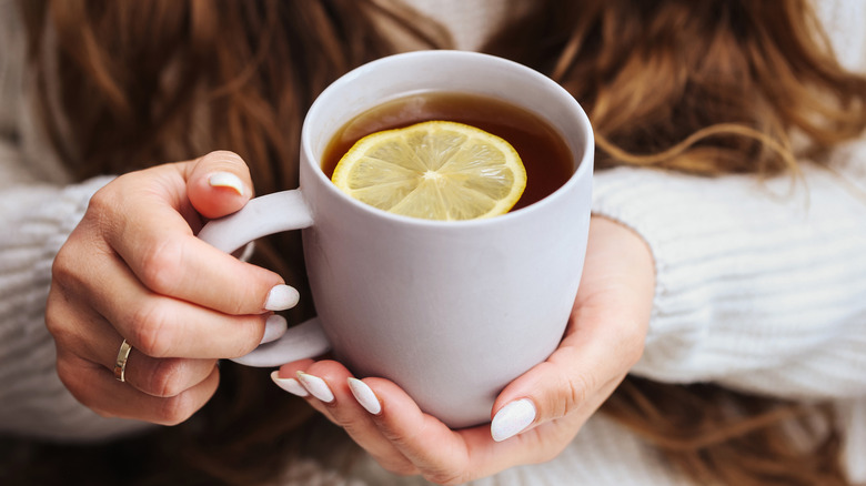 person holding cup of tea with lemon slice
