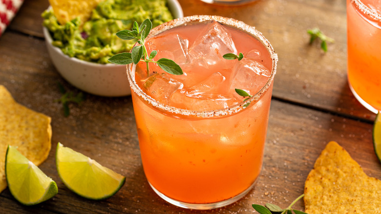 spicy grapefruit cocktail with guacamole, chips and lime on a wooden tabletop.