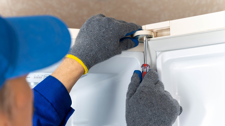 A man using a screwdriver to replace the hinge on a freezer door