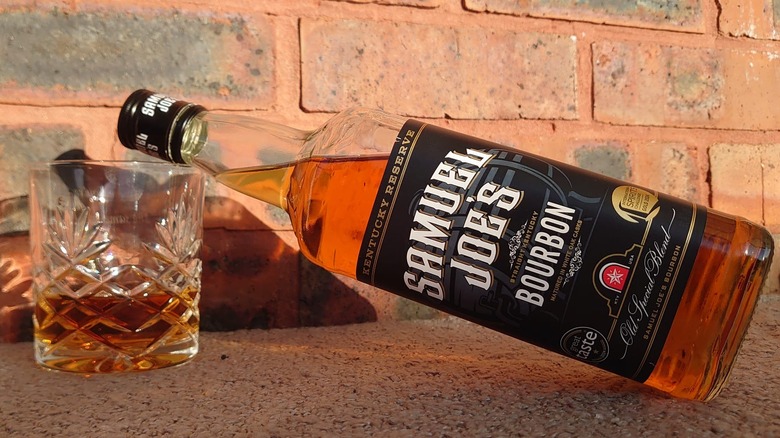 A bottle of Samuel Joe's bourbon laying on the rim of a filled whiskey tumbler