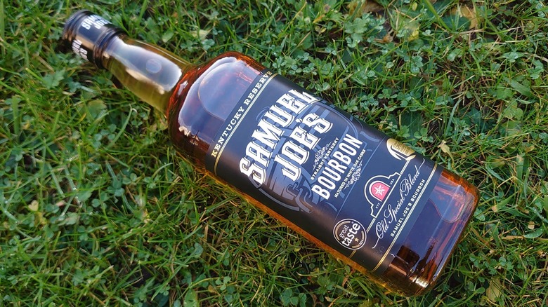 An overhead shot of a bottle of Samuel Joe's laying diagonally on a patch of grass
