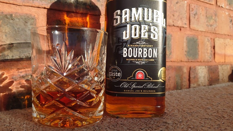 A close shot of a filled glass of Samuel Joe's bourbon alongside its bottle