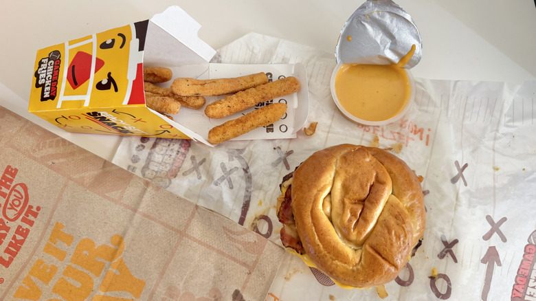 Top view of Game Day Pretzel Burger, Chicken Fries, and nacho sauce on a table