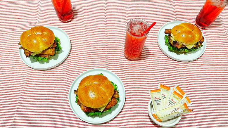 Three of Chick-fil-A's new sandwiches arrange over a striped tablecloth with strawberry hibiscus drinks