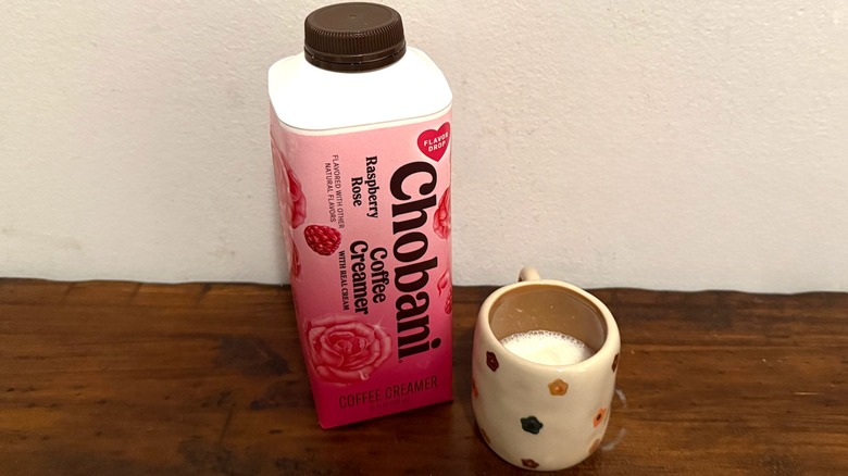 container of Chobani Raspberry Rose coffee creamer next to a small cup filled with cream