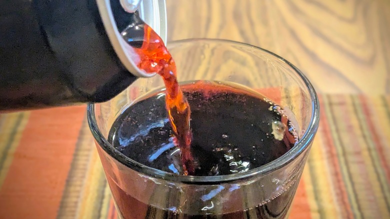 A close-up of red soda pouring from a can into a glass