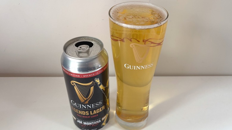 Open can of Guinness Legends Lager next to full pint glass of lager on white table