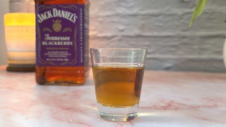 Close-up of shot glass filled with Jack Daniel's Tennessee Blackberry Whiskey, bottle and candle in background