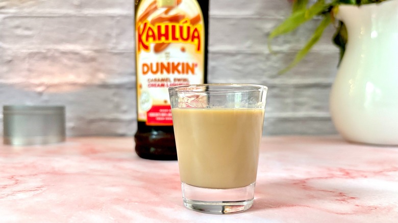 Shot glass of Kahlúa Dunkin Caramel Swirl Cream Liqueur with bottle in the background