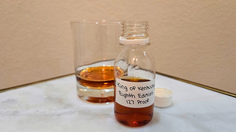 Sample bottle of King of Kentucky's limited-edition 2025 expression bourbon with rocks glass in background