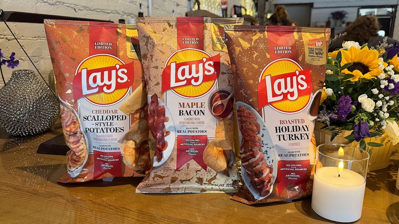 Three bags of Lay's holiday flavors on wooden table next to candle and flowers