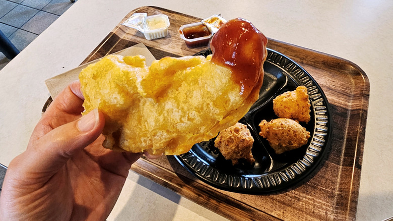 A person holding Long John Silver's chicken strip dipped in barbecue sauce