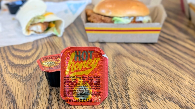 Two cups of McDonald's Hot Honey Sauce with menu items in the background