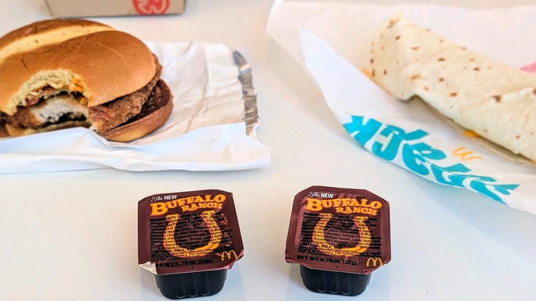 Two seals cups of McDonald's Buffalo Ranch on table with two Buffalo Ranch menu items in the background