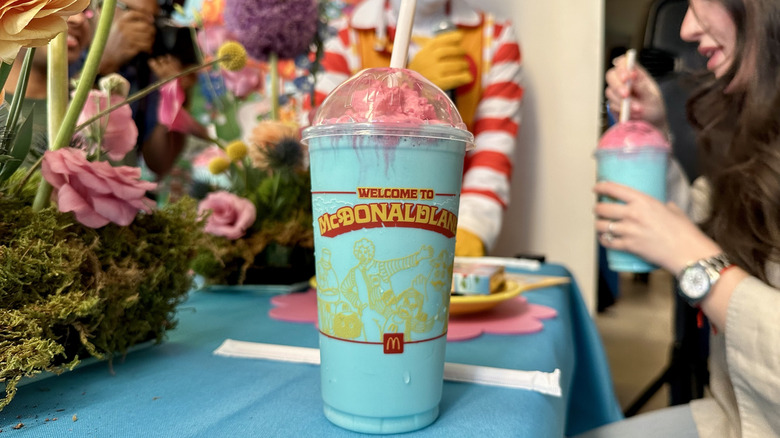 A Mt. McDonaldland Shake on a table with floral center pieces and Ronald McDonald in the background