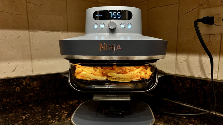 Fries cooking inside of a glass Ninja air fryer basket