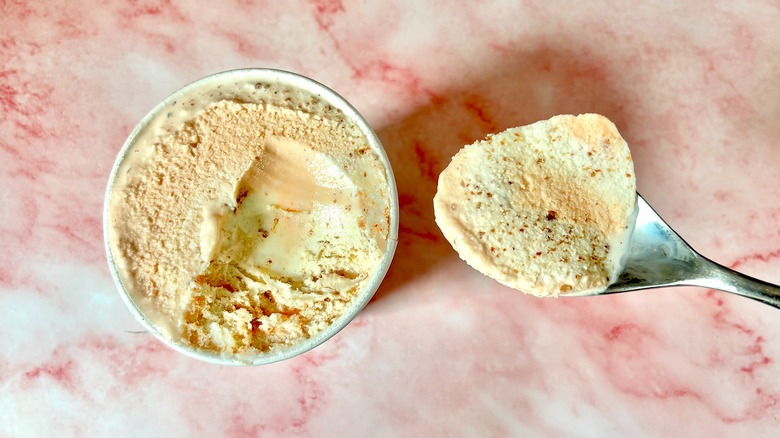 Top-down view of Melon and Prosciutto Salt & Straw pint next to spoon on pink marble surface