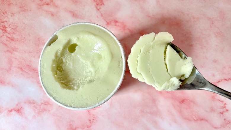 Top-down view of Pickled Cucumber Sorbet Salt & Straw pint next to spoon on pink marble surface