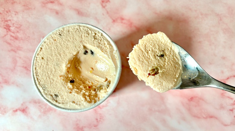 Top-down view of Tomato Gelato with Olive Brittle Salt & Straw pint next to spoon on pink marble surface
