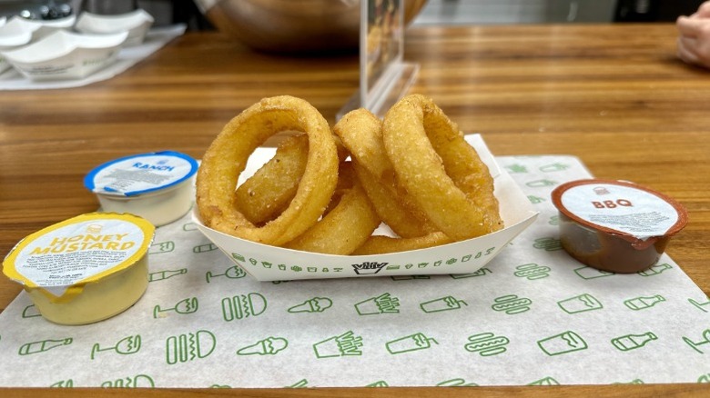 Shake Shack's onion rings with ranch, BBQ, and honey mustard dipping sauces on a patterned paper placemat