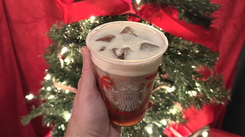 Cold Brew with Eggnog Cold Foam in hand, in front of a tree