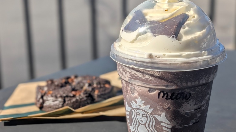 A close-up of a Starbucks Black Cat Frappuccino and a Venti Black Night Cookie in the background