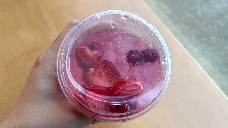 Top-down shot of hand holding Starbucks Pink Cannon Ball Drink over table in cafe