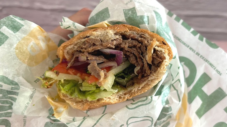 Hand holding Subway steak avocado sandwich in wrapper