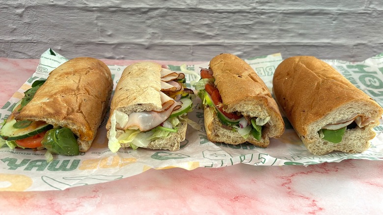 Four Subway sandwiches on wrapper on pink table