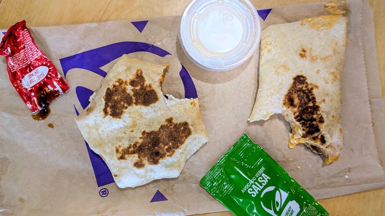 A Cantina Chicken Rolled Quesadilla and a Crunchwrap Slider with bites taken out next to cups and packets of condiments