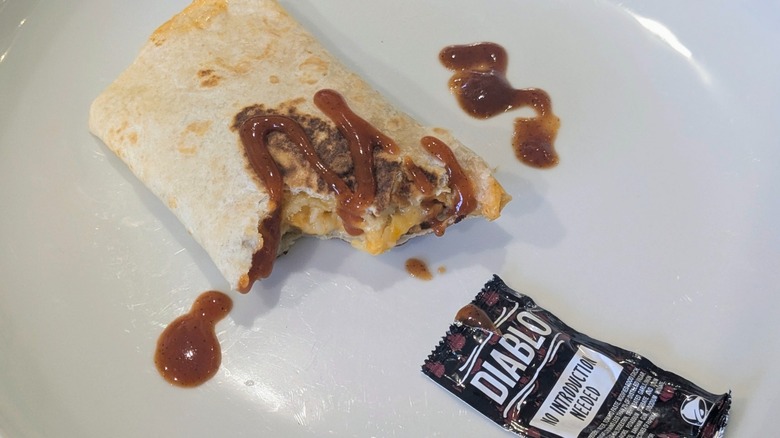 A half-eaten Cantina Chicken Rolled Quesadilla with a packet of Diablo sauce on a white plate