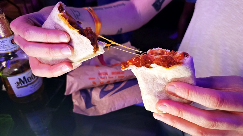 Two hands pulling apart the chili cheese burrito
