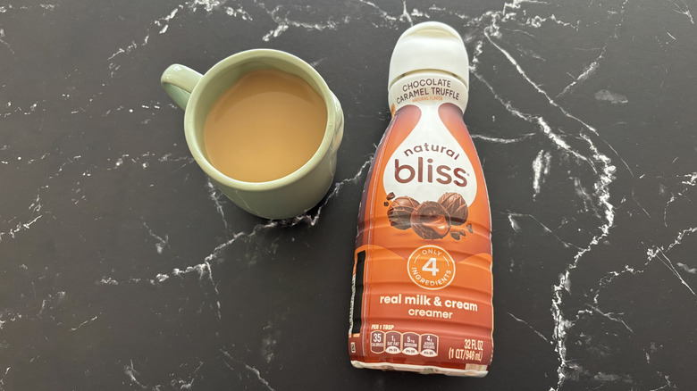 Cup of coffee next to Natural Bliss chocolate caramel truffle creamer bottle