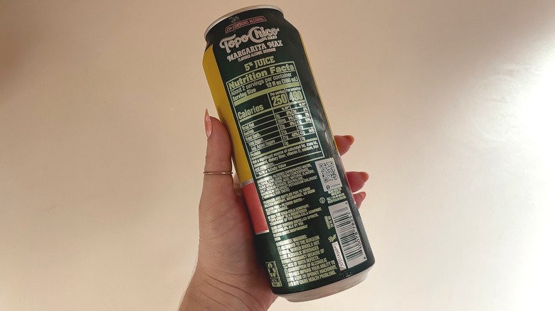 Hand holding can of Topo Chico Margarita Max showing nutrition label over white table