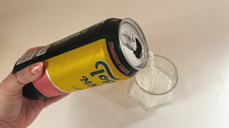 Hand pouring can of Topo Chico Margarita Max into glass on white table