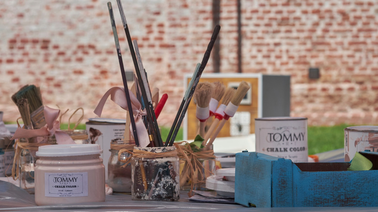 A table loaded with craft supplies including paint brushes and vintage paint