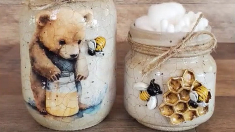 Two Mason jars painted to look like cracked porcelain with a bear design on one and a honeycomb and bee design on the other.