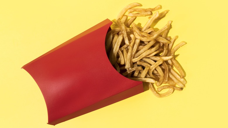 A red carton of French fries spilling with a yellow background