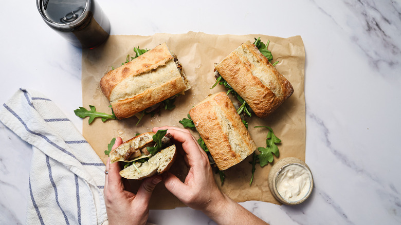 Hands holding one of four ribeye steak sandwiches on parchment