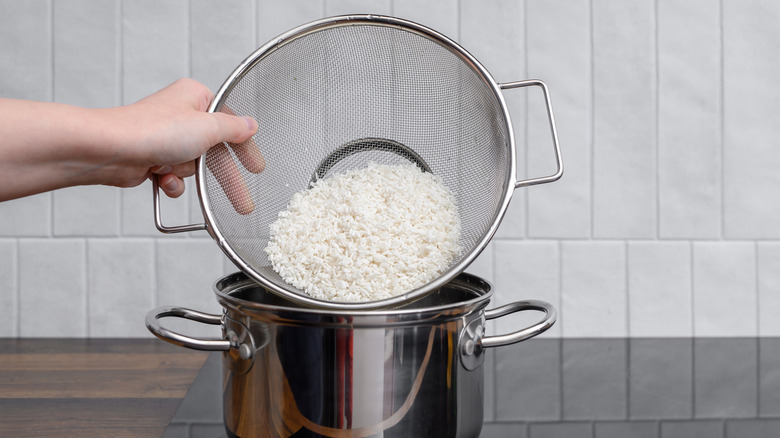 A strainer of rice being poured into a pot