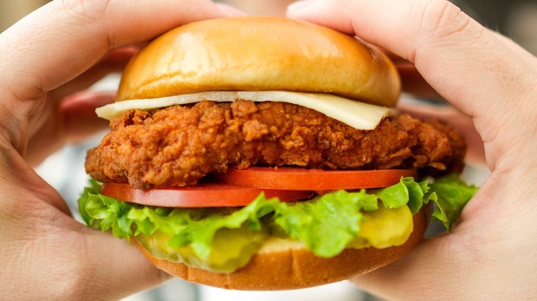 Hands holding chicken sandwich at restaurant