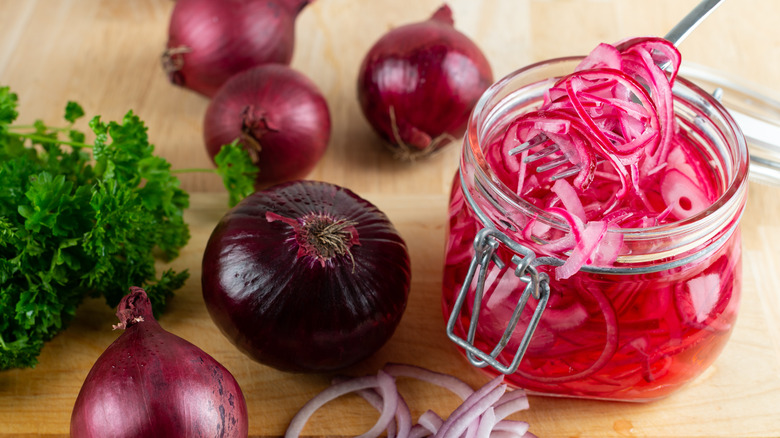 An open jar of homemade pickled red onions on a counter with a fork inside