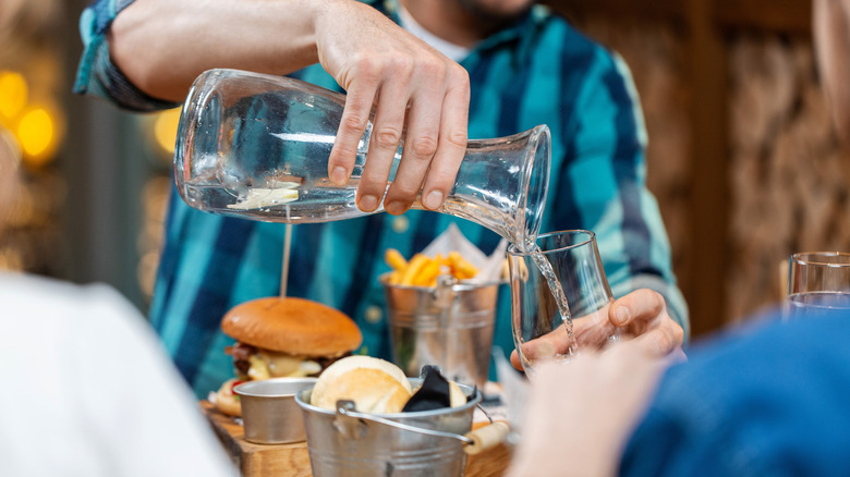 man having dinner at restaurant, close up of hand pouring water from jug to glass