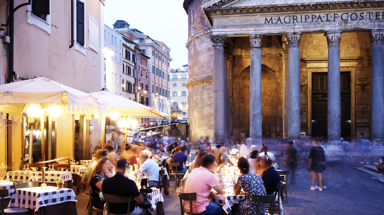 people dining outside at night in a Piazza by ancient monument