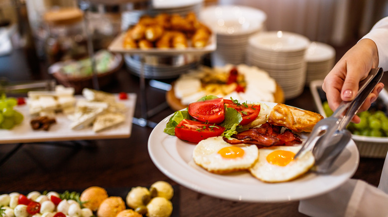 a plate being filled with eggs and tomatoes at a breakfast buffet