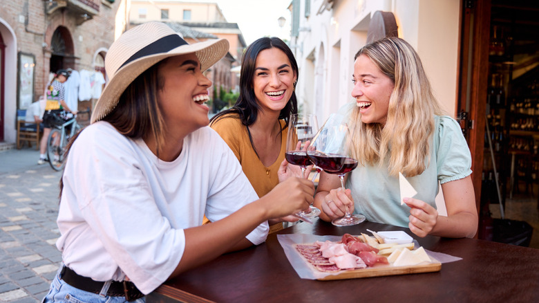 Three women enjoying italian meats and red wine at an outdoor table.