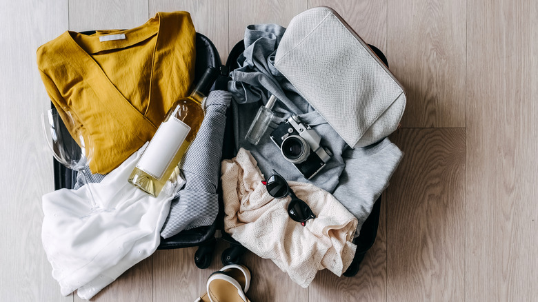 Various clothes and a bottle of wine in opened suitcase