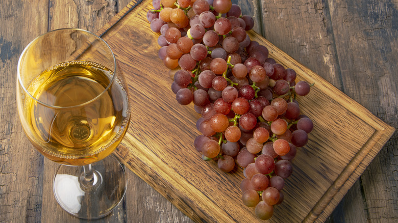 A glass of gewürztraminer wine with a cluster of grapes on a wooden tray